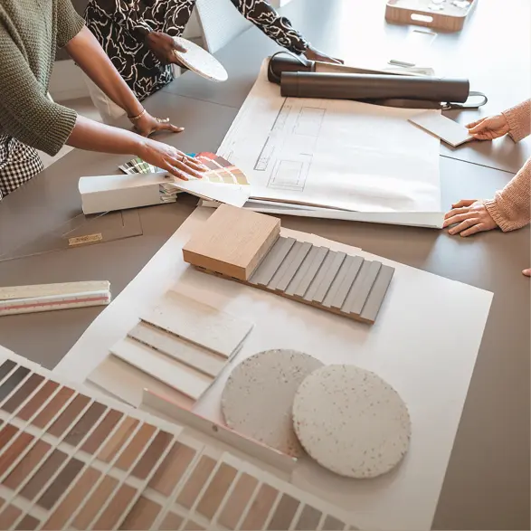 Hände zeigen auf Farb- und Materialmuster neben einem Küchenplan, Holzproben und Platten liegen auf einem Tisch